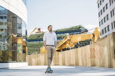 Geschäftsmann fährt Skateboard auf einer Baustelle in der Stadt - JOSEF00579