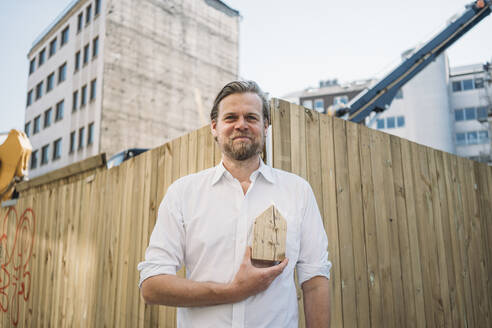 Geschäftsmann mit Holzhausmodell auf einer Baustelle in der Stadt - JOSEF00584