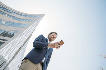 Smiling businessman using smartphone in the city - JOSEF00607