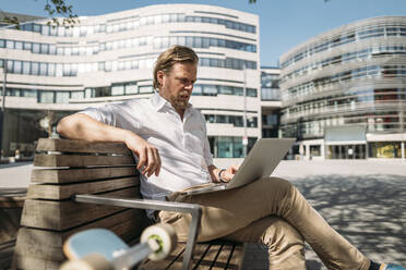 Businessman sitting on a bench in the city using laptop - JOSEF00608