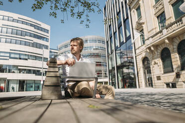 Businessman sitting on a bench in the city using laptop - JOSEF00610