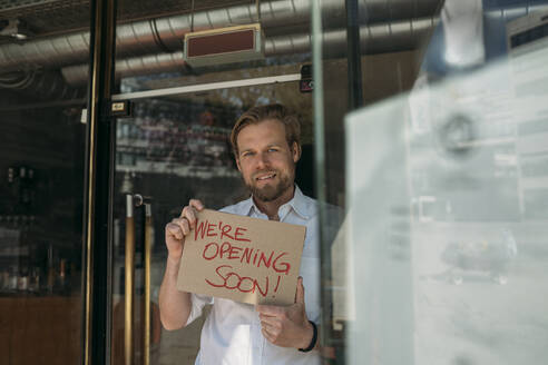 Shopkeeper holding cardboard with opening announcement in the city - JOSEF00615