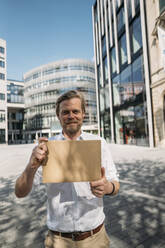Porträt eines lächelnden Mannes mit leerem Karton in der Stadt - JOSEF00620
