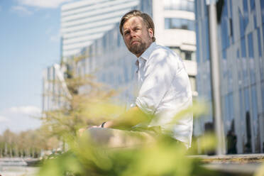 Businessman having a break in the city sitting on a wall - JOSEF00638