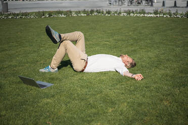 Geschäftsmann im Gras liegend neben einem Laptop - JOSEF00657