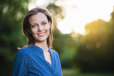 Portrait of smiling woman standing at park - DIGF10900