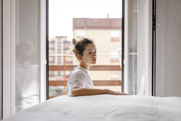 Side view of thoughtful young woman looking away while sitting by bed at home - TCEF00647