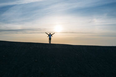 Businessman standing with arms outstretched on hill against sky during sunset - MOEF02882