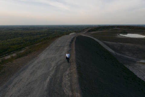 Älterer Geschäftsmann, der auf einem Fußweg über einen Hügel gegen den Himmel bei Sonnenuntergang läuft, lizenzfreies Stockfoto