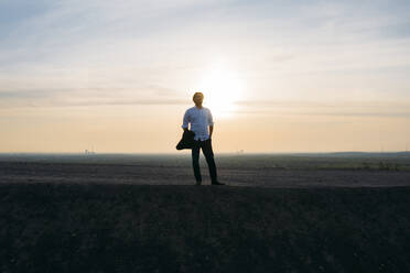 Männlicher Unternehmer steht auf einem Hügel gegen den Himmel bei Sonnenuntergang - MOEF02888