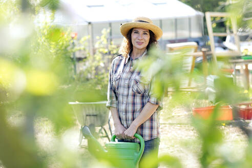 Portrait of smiling female farmer holding watering can while standing at community garden - FLLF00480