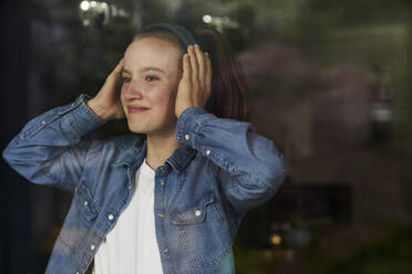 Lächelndes junges Mädchen, das zu Hause über Kopfhörer Musik hört - AUF00496