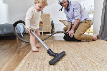 Mann schaut auf niedliches Kleinkind Sohn Reinigung Teppich mit Staubsauger im Wohnzimmer zu Hause - FSF01072