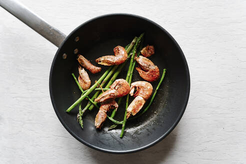 Overhead view of grilled prawns and asparagus on frying pan - JMHMF00042