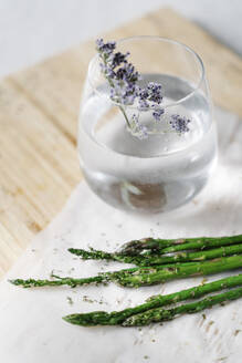 Green asparagus and jug with water and flower on wooden cutting board - JMHMF00050