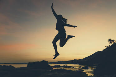 Silhouette of jumping woman at beach during sunset - DMGF00085