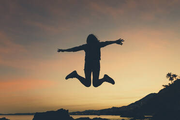 Silhouette of jumping woman at beach during sunset - DMGF00086