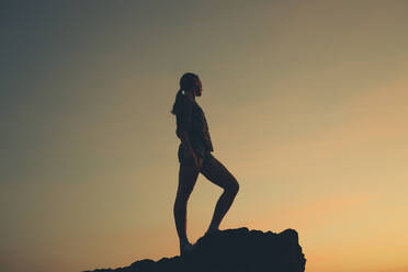 Frau auf einem Bein stehend am Strand bei Sonnenuntergang - DMGF00088