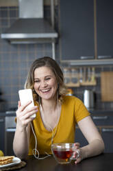 Glückliche Frau, die in der Küche zu Hause einen Videochat mit ihrem Smartphone führt - VPIF02464