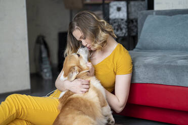 Woman cuddling with her dog in living room at home - VPIF02466