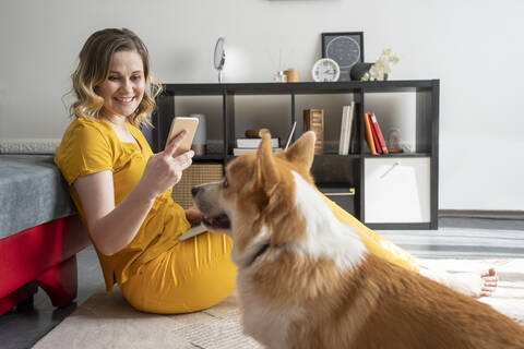 Frau mit Hund benutzt Smartphone im Wohnzimmer zu Hause, lizenzfreies Stockfoto