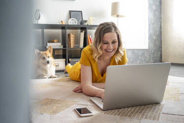 Glückliche Frau mit Hund, die einen Laptop im Wohnzimmer zu Hause benutzt - VPIF02471