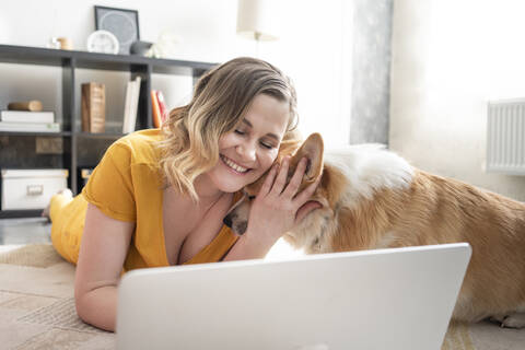 Frau mit Hund benutzt Laptop im Wohnzimmer zu Hause, lizenzfreies Stockfoto