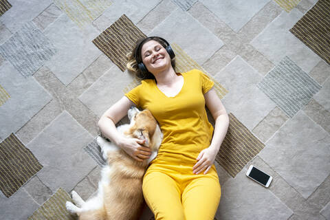 Happy woman with headphones cuddling with her dog in living room at home stock photo