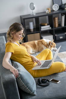 Frau mit Hund benutzt Laptop im Wohnzimmer zu Hause - VPIF02480