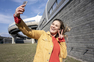 Happy woman with windswept hair taking a selfie at a brick wall - VPIF02498