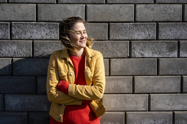Smiling woman standing at a brick wall listening to music with headphones - VPIF02500