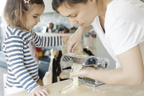 Nettes Mädchen schaut Mutter an, die Spaghetti mit Hilfe von Geräten in der Küche zubereitet - JCZF00067