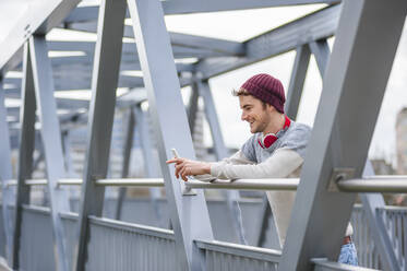 Stylischer junger Mann mit Smartphone auf einer Brücke - DIGF10905