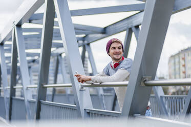 Stylischer junger Mann mit Smartphone auf einer Brücke - DIGF10906