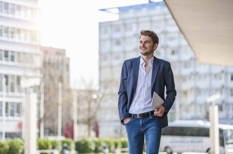 Smiling young businessman with tablet walking in the city stock photo