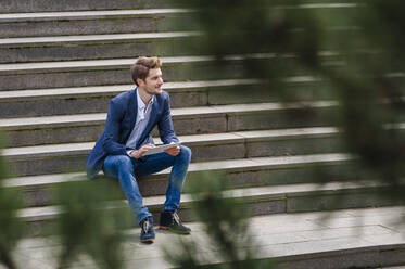 Junger Geschäftsmann sitzt auf einer Treppe und benutzt ein Tablet - DIGF10930