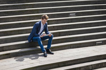 Junger Geschäftsmann sitzt auf einer Treppe und benutzt ein Tablet - DIGF10931