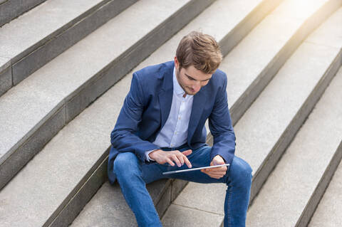 Junger Geschäftsmann sitzt auf einer Treppe und benutzt ein Tablet, lizenzfreies Stockfoto