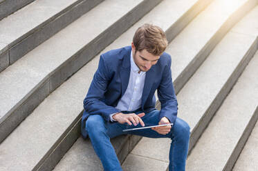Junger Geschäftsmann sitzt auf einer Treppe und benutzt ein Tablet - DIGF10932
