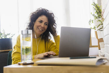 Lächelnde Frau mit Laptop am Schreibtisch im Home Office - ERRF03768