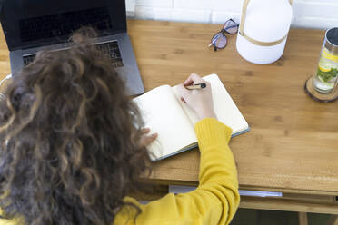 Woman working at desk in home office taking notes - ERRF03774