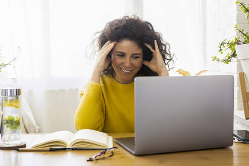 Lächelnde Frau mit Laptop am Schreibtisch im Home Office - ERRF03779