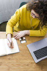 Woman working at desk in home office taking notes - ERRF03784
