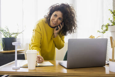 Frau am Telefon bei der Arbeit am Schreibtisch im Heimbüro - ERRF03792