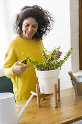 Woman at home wearing headphones and pruning plants - ERRF03801