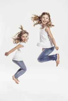 Portrait of two barefoot sisters jumping in the air in front of white background - SDAHF00938