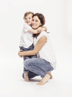 Portrait of happy mother and her little son hugging each other in front of white background - SDAHF00941
