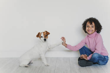 Porträt eines lächelnden kleinen Mädchens, das mit seinem Hund auf dem Boden sitzt und Pfötchen gibt - EBBF00003