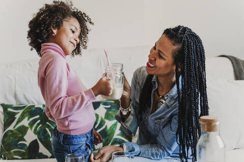 Happy mother and her little daughter with glass of milk at home stock photo