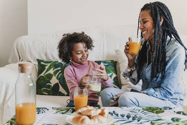 Glückliche Mutter und ihre kleine Tochter trinken Smoothie und Saft zu Hause - EBBF00012